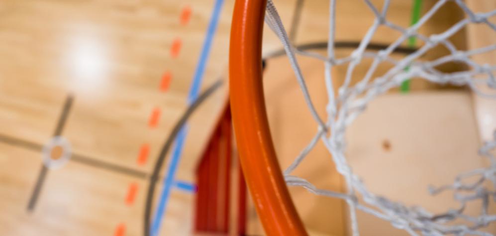 Nahaufnahme eines Basketballkorbs mit Netz über einem aufgezeichneten Basketballfeld aus Holz.