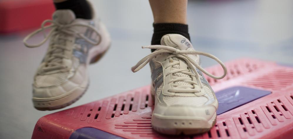 Nahaufnahme eines Sportschuhs auf einem pinken Stepper im Fitnessstudio.
