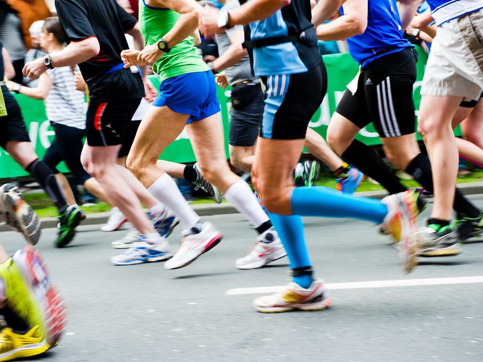 Bunte Laufschuhe rennen in einem Marathon, während Zuschauer im Hintergrund auf der Strecke stehen.